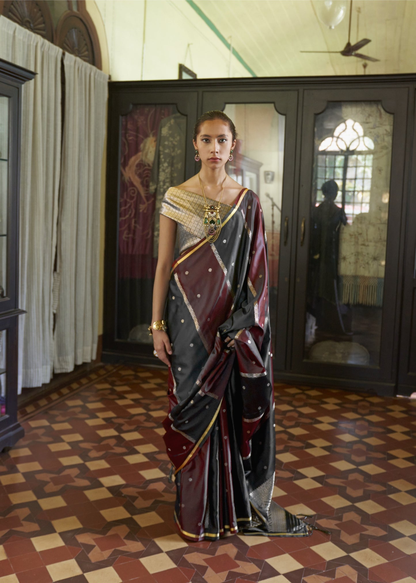 Woman in a traditional saree standing in a room with patterned floor and decorative walls.