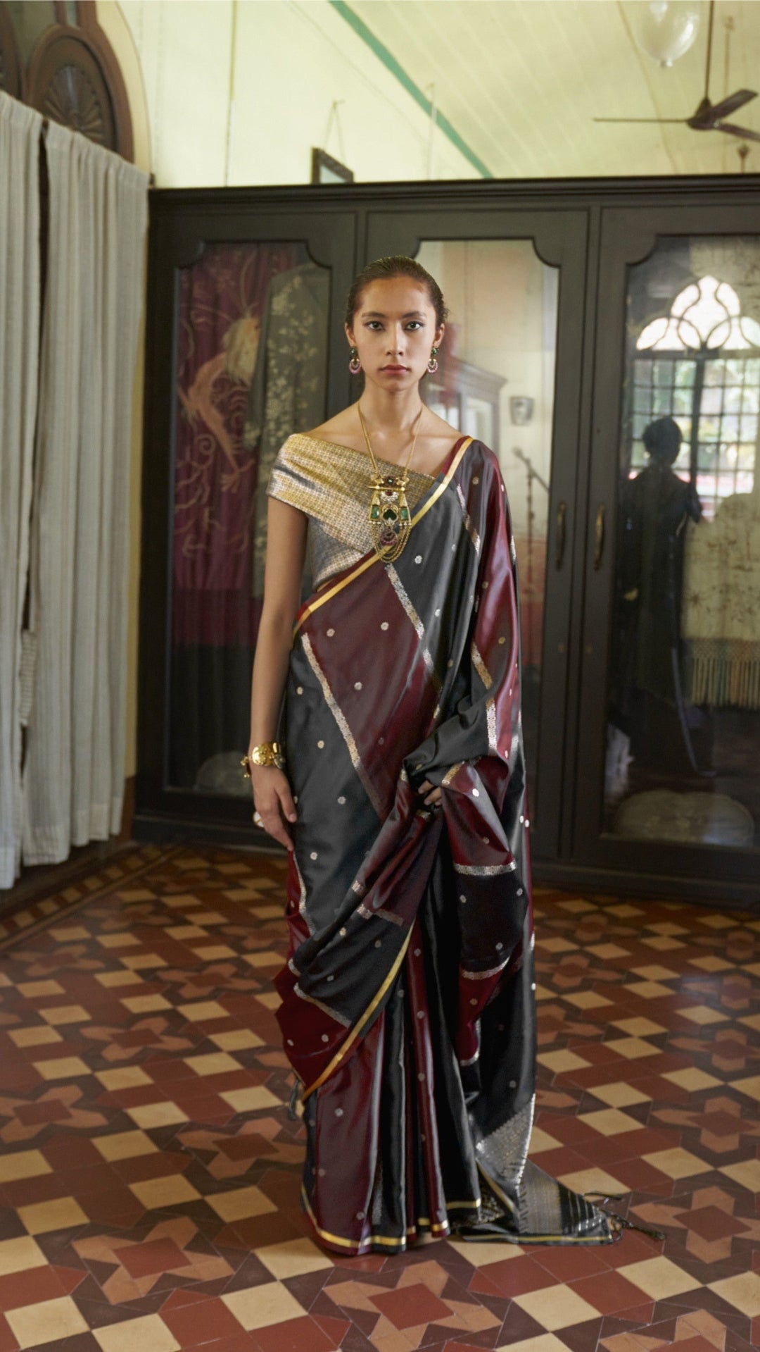 Woman in a traditional saree standing in a room with patterned floor and decorative walls.