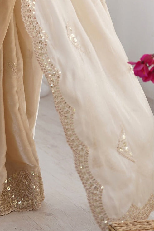 Woman wearing a beige saree with intricate designs in a minimal indoor setting.