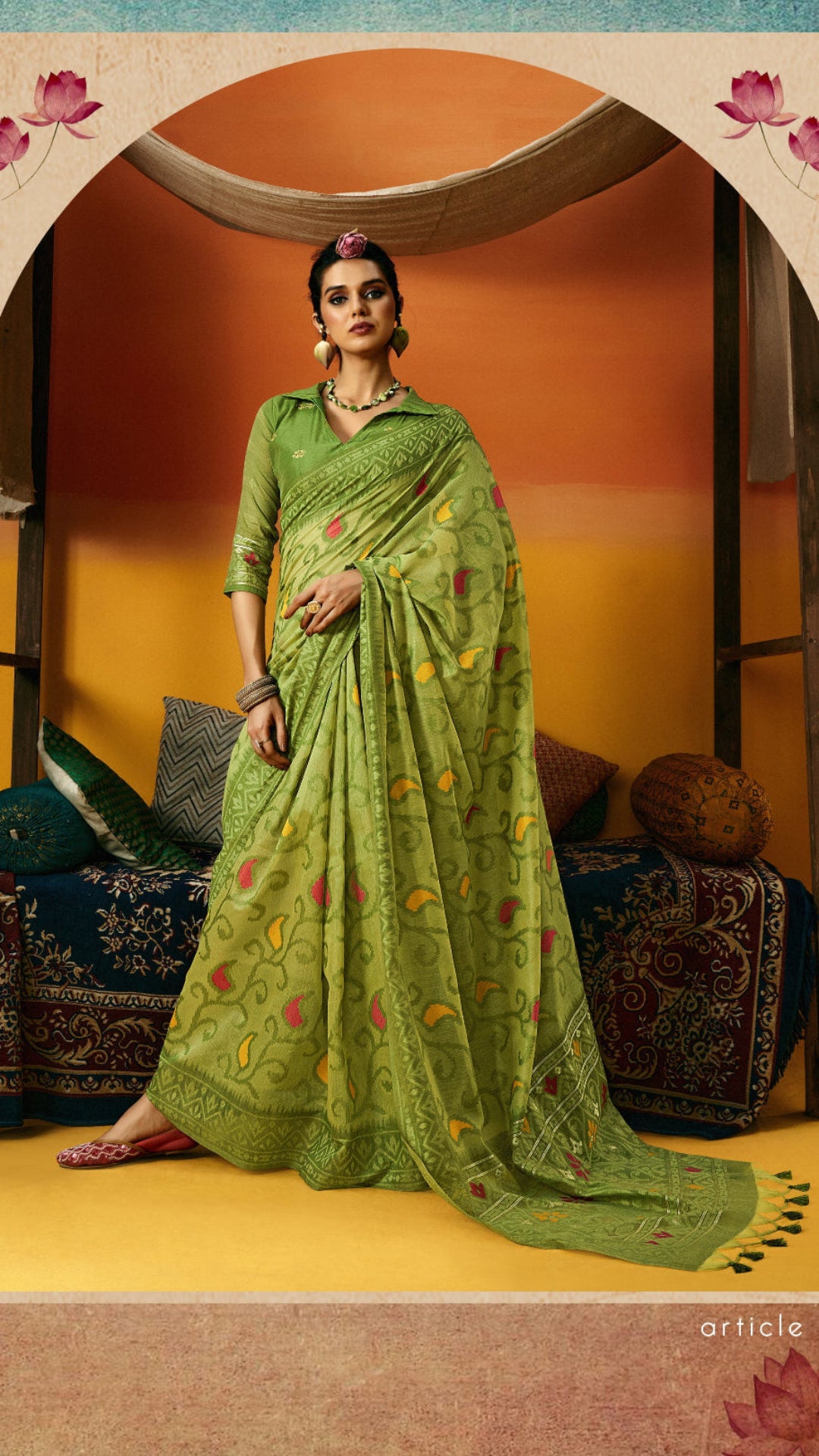 Woman in a green saree with floral patterns standing in a decorated room.