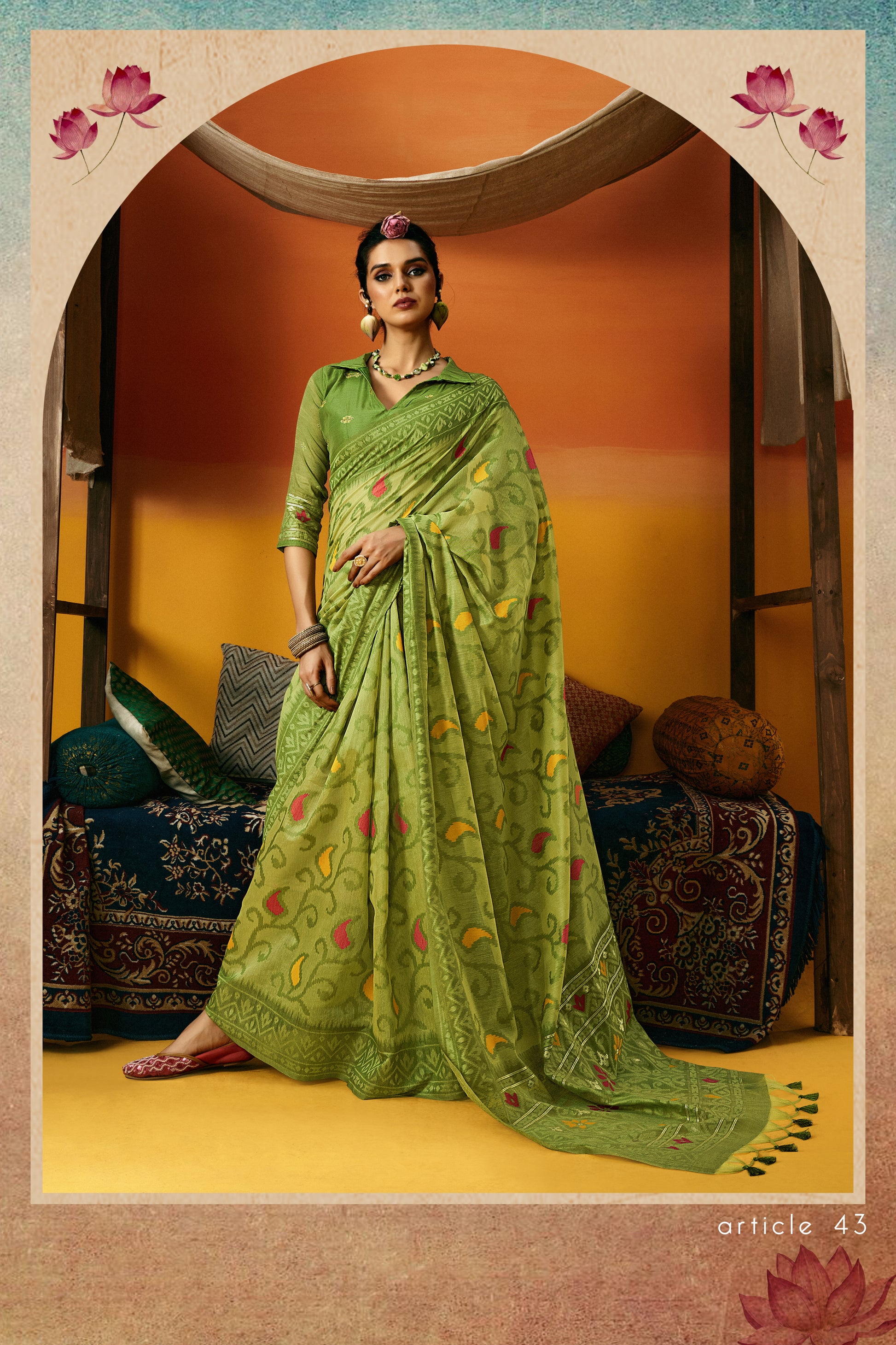 Woman in a green saree with floral patterns standing in a decorated room.
