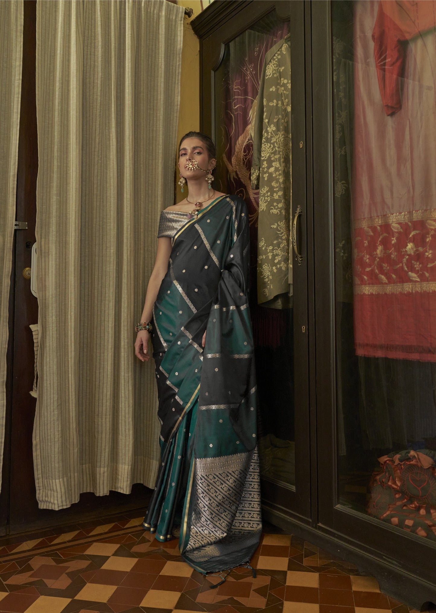 Woman in a saree standing in front of a wardrobe with various clothes on display.