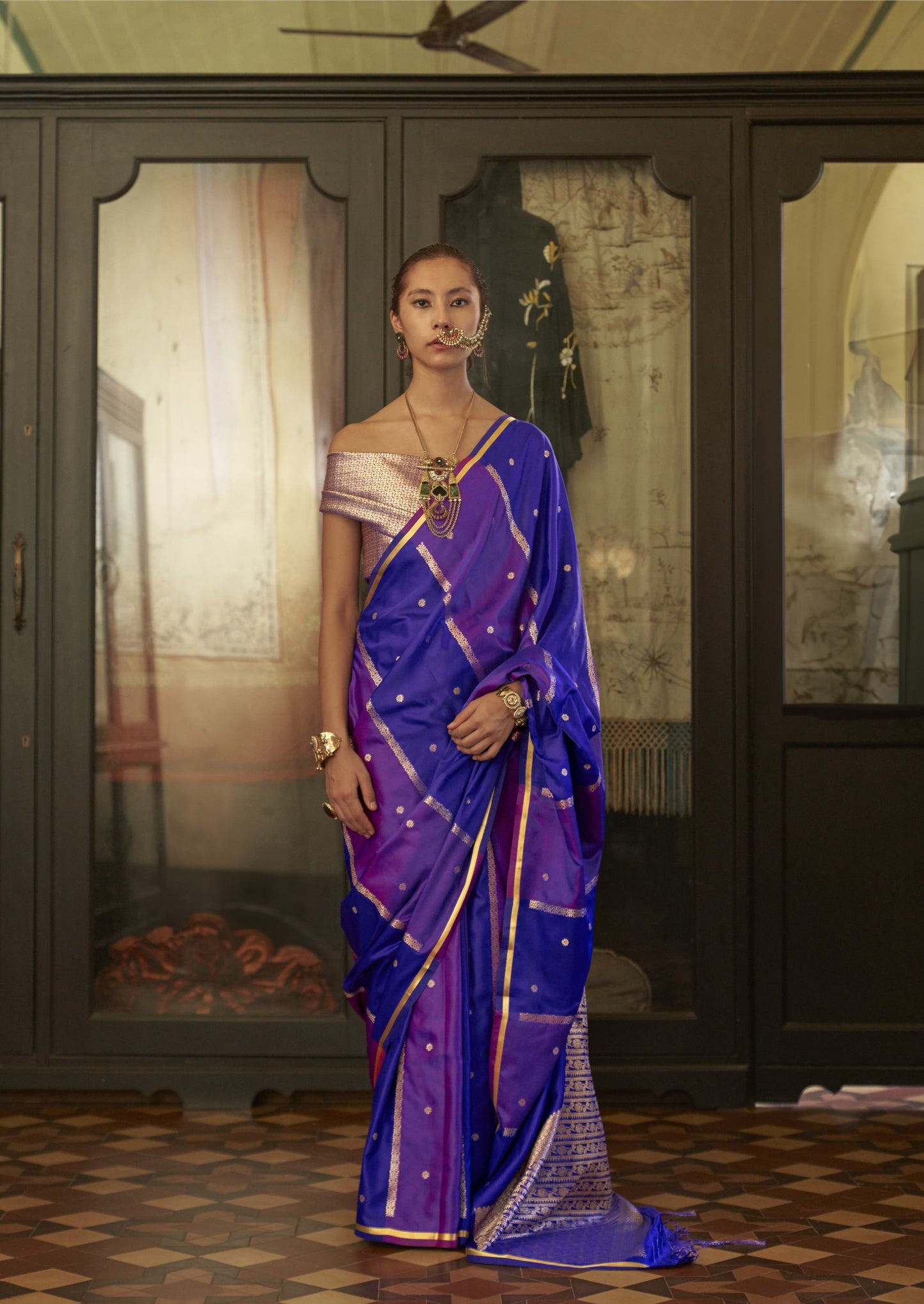 Woman in a purple saree standing in a room with decorative elements.
