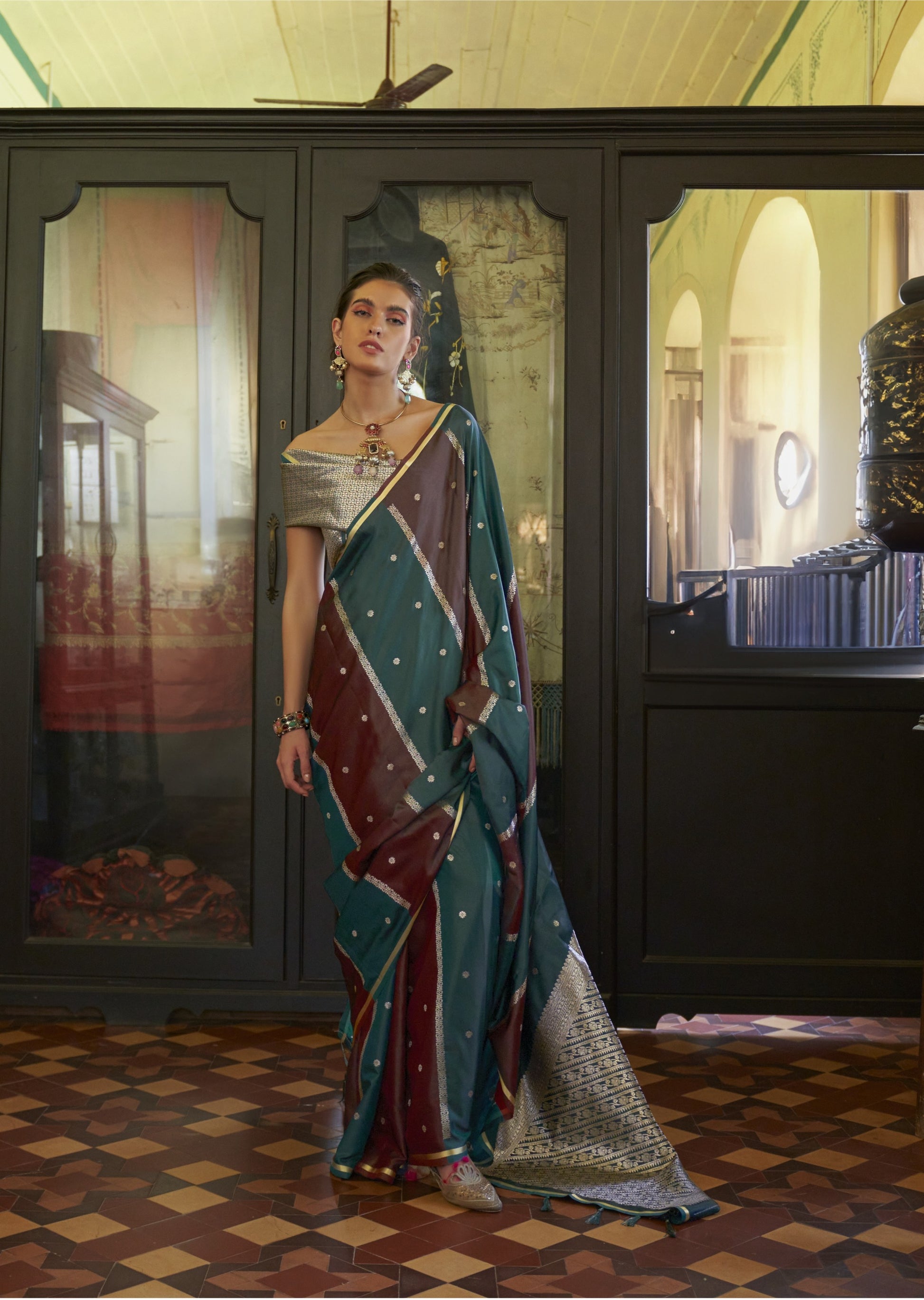 Woman in a traditional saree standing in a room with decorative walls and a checkered floor.