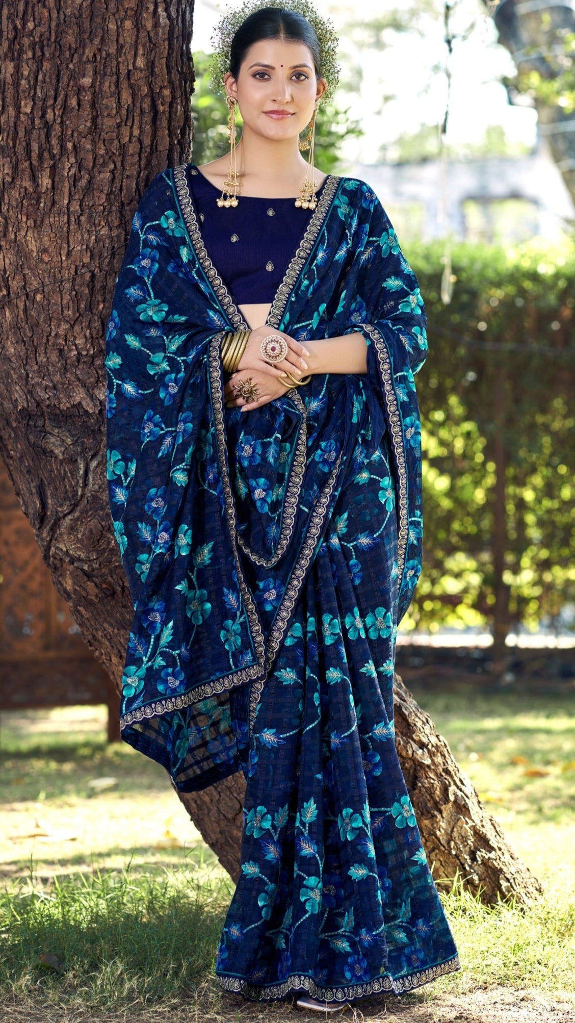Woman wearing a blue floral saree with a matching blouse outdoors.