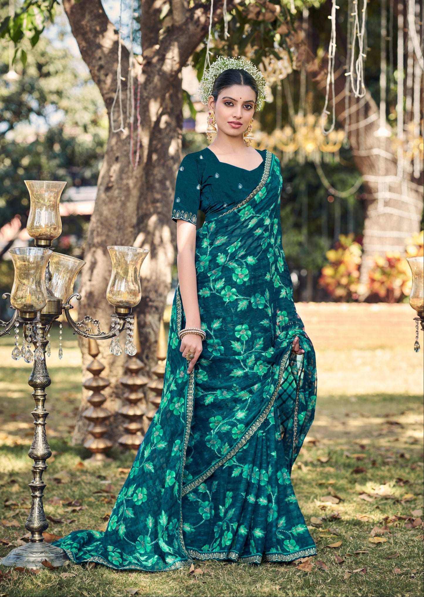Woman in a green saree with floral patterns standing outdoors.