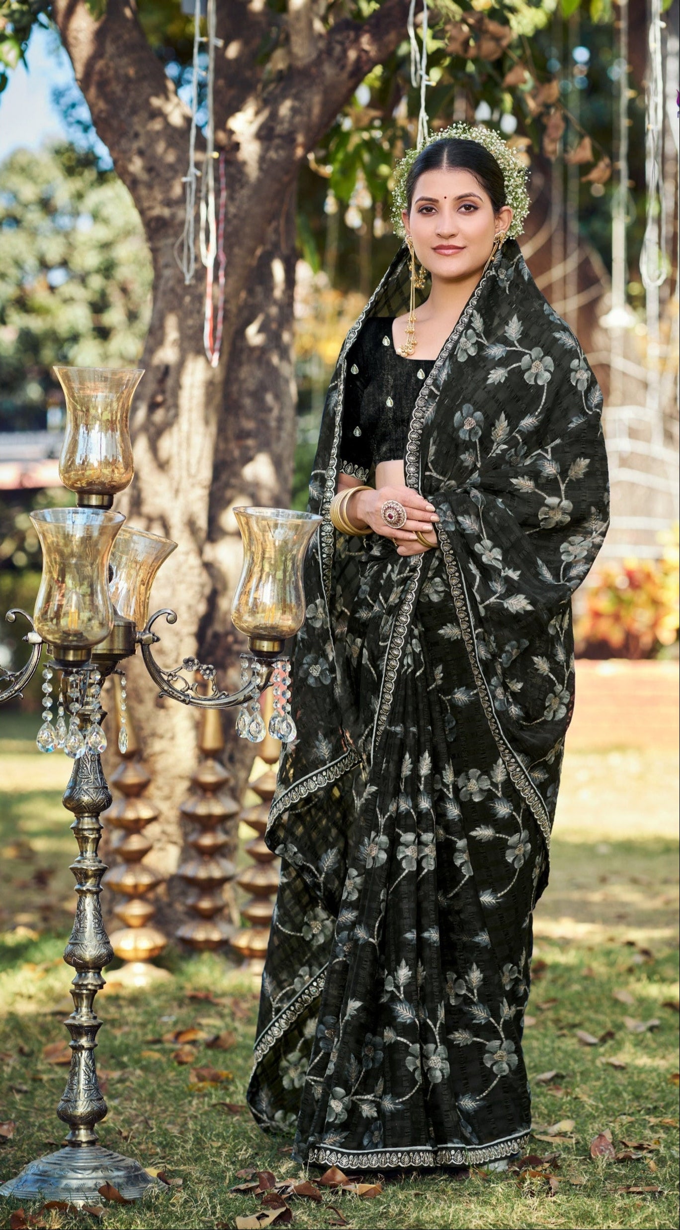 Woman in a black saree with white patterns standing outdoors with decorative elements.