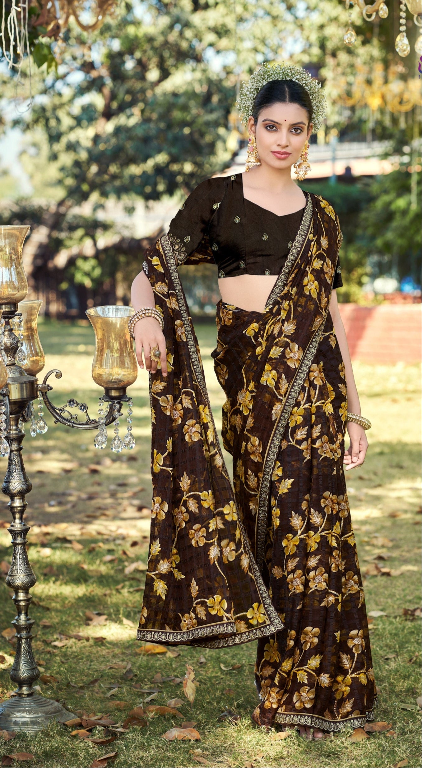 Woman in a traditional brown and gold saree standing outdoors with greenery in the background