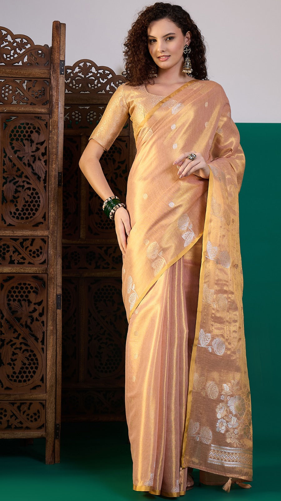 Woman wearing a gold saree with a decorative wooden panel in the background