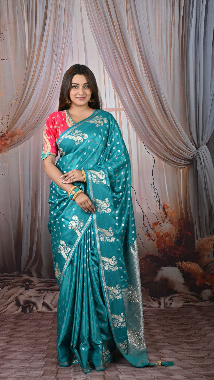 Woman wearing a teal saree with white patterns against a decorative curtain background