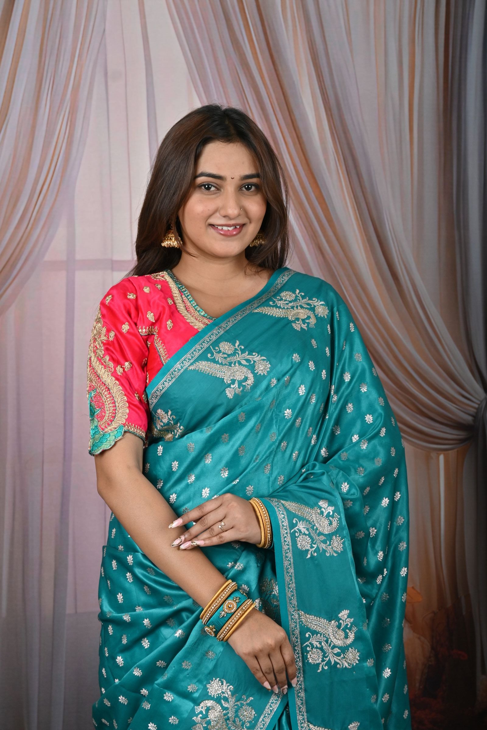 Woman wearing a teal saree with gold patterns, posing against a neutral background.