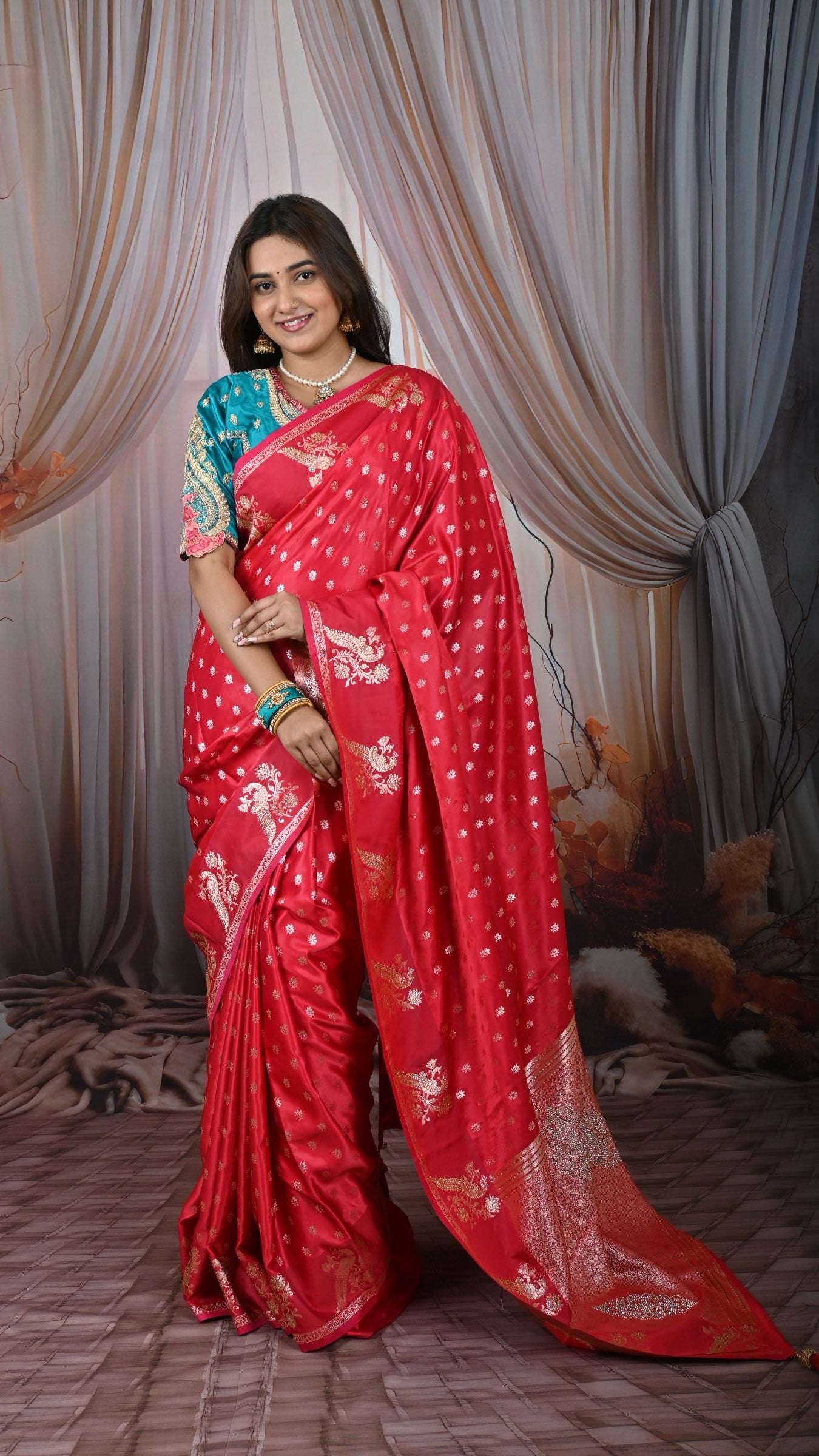 Woman in a red saree with white patterns standing in front of a large mirror.