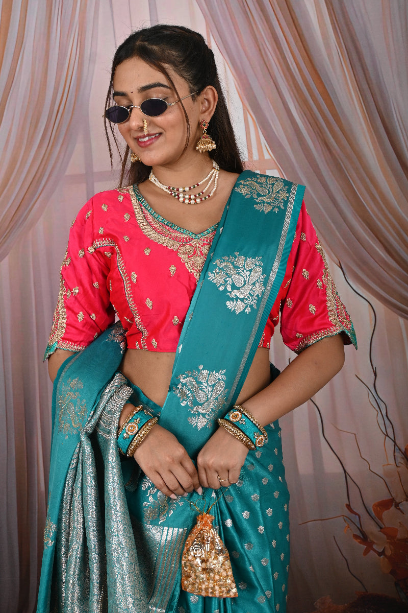 Woman in a pink blouse and teal saree with gold jewelry against a draped fabric background