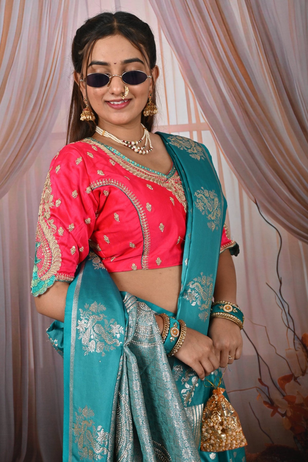 Woman in a pink blouse and blue saree with gold embroidery against a patterned curtain.