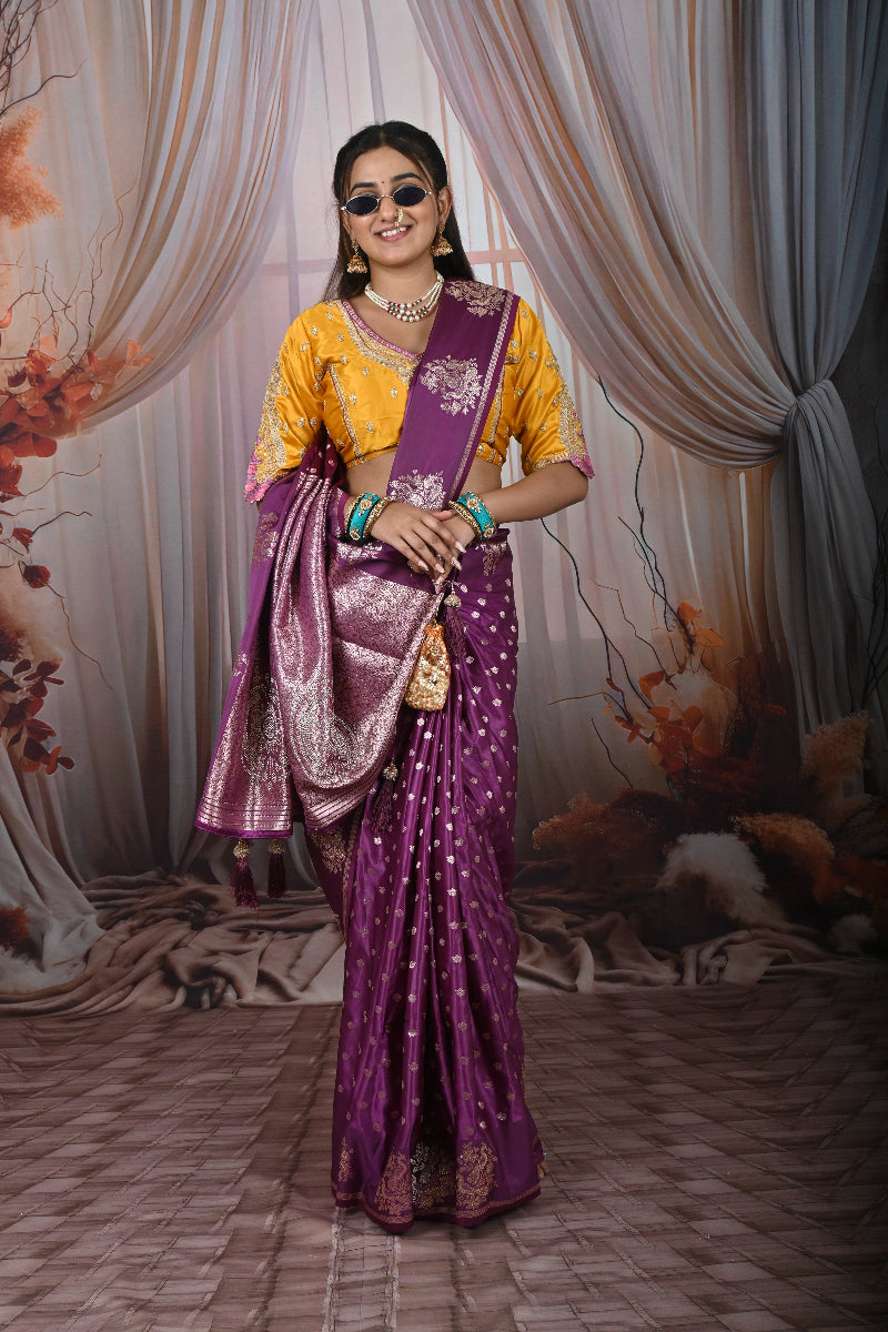 Woman in a purple and yellow saree standing in front of draped curtains.