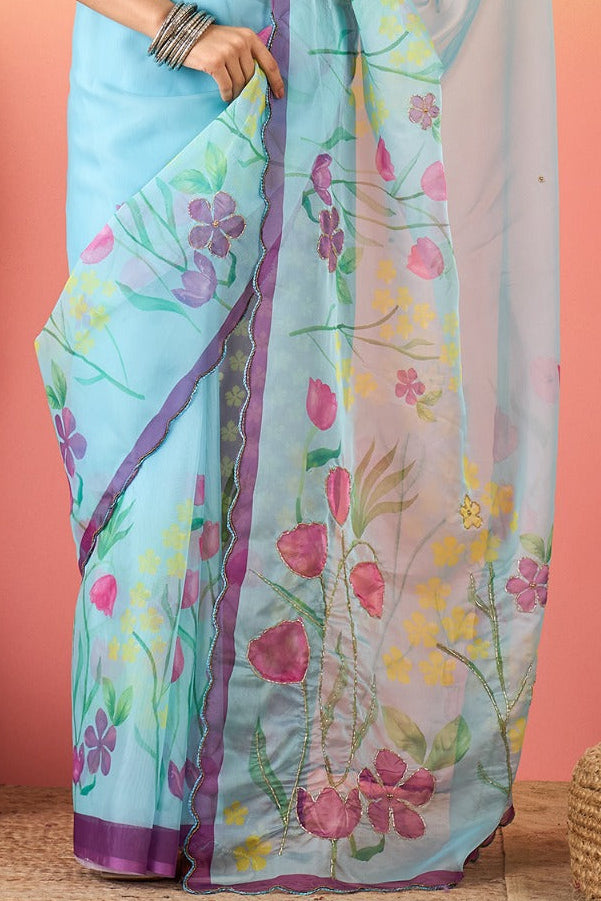 Woman wearing a light blue floral saree with a pink blouse against a gradient background