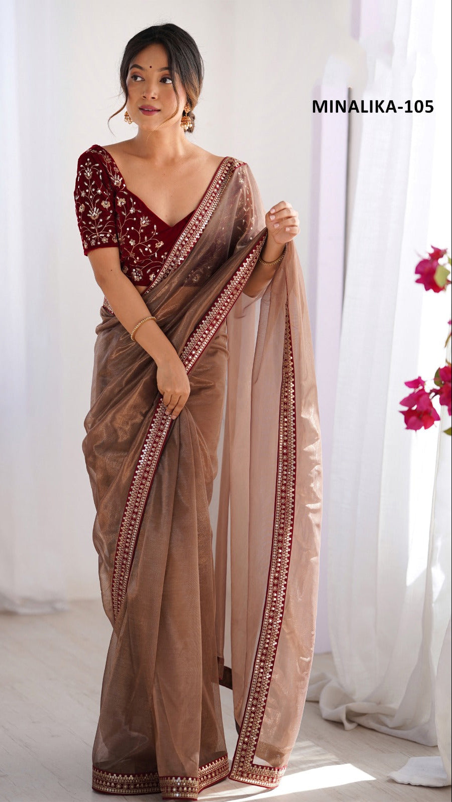 Woman wearing a brown saree with a red blouse against a white curtain background
