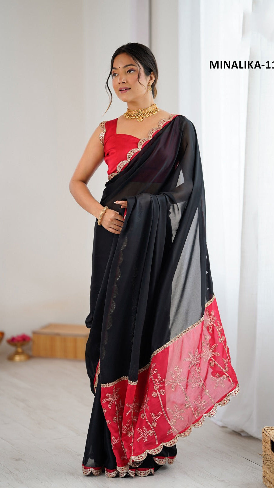 Woman wearing a black and red saree with a white curtain background