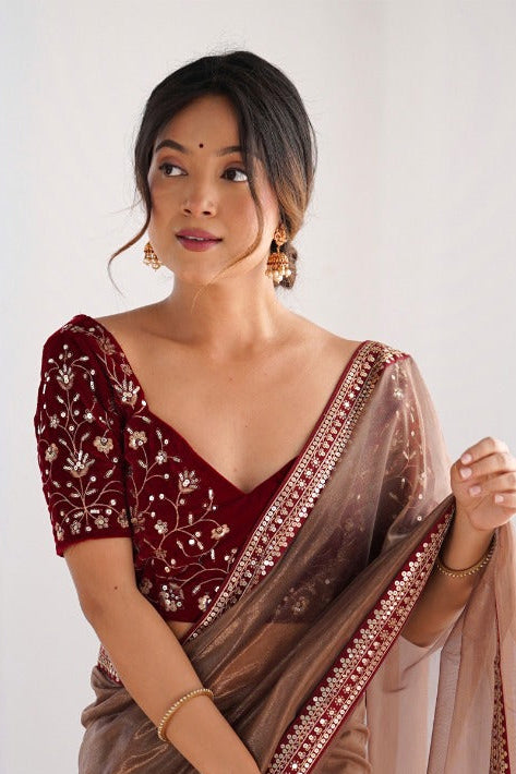 Woman wearing a brown saree with a red blouse against a white curtain background