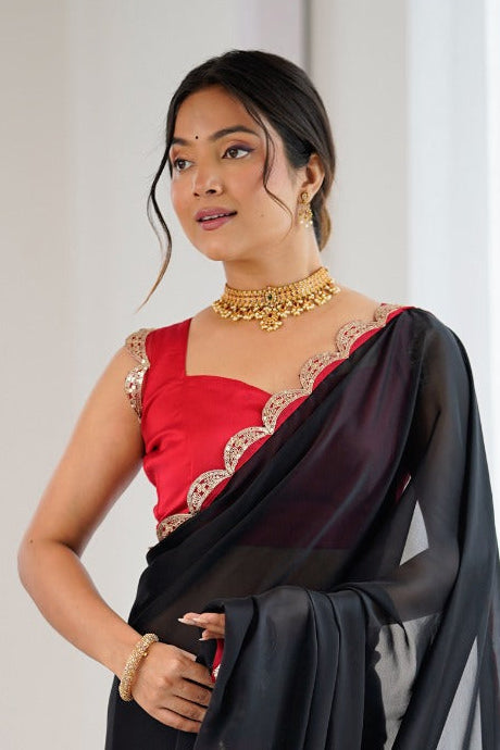 Woman wearing a black and red saree with a white curtain background