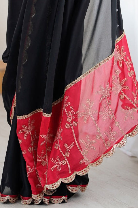 Woman wearing a black and red saree with a white curtain background