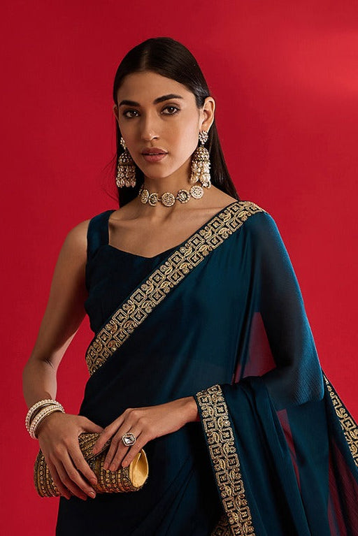 Woman wearing a blue saree with gold border on a red background