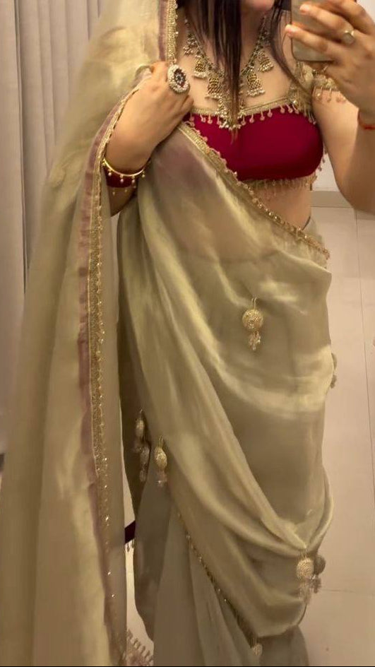 Woman taking a mirror selfie wearing a traditional outfit with a red blouse and beige saree.