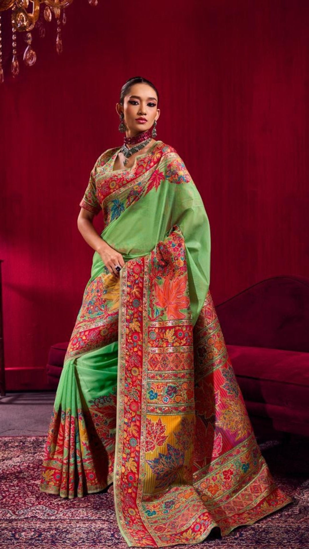 Woman wearing a green saree with a colorful pattern against a red background