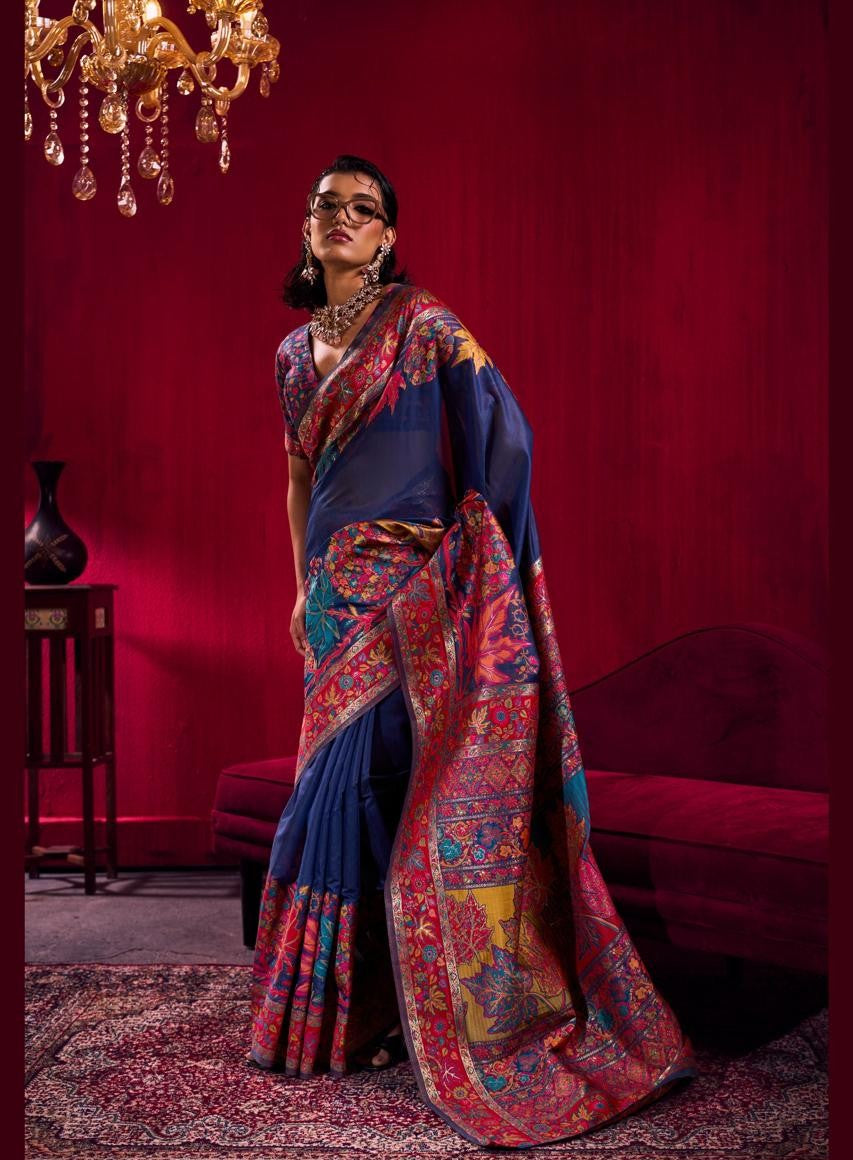 Woman in a blue and red saree standing in a room with red walls and a chandelier.