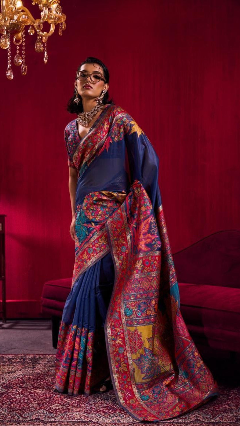 Woman in a blue and red saree standing in a room with red walls and a chandelier.