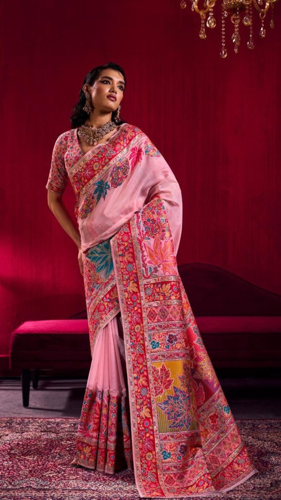 Woman wearing a pink saree with intricate patterns in a room with red walls.