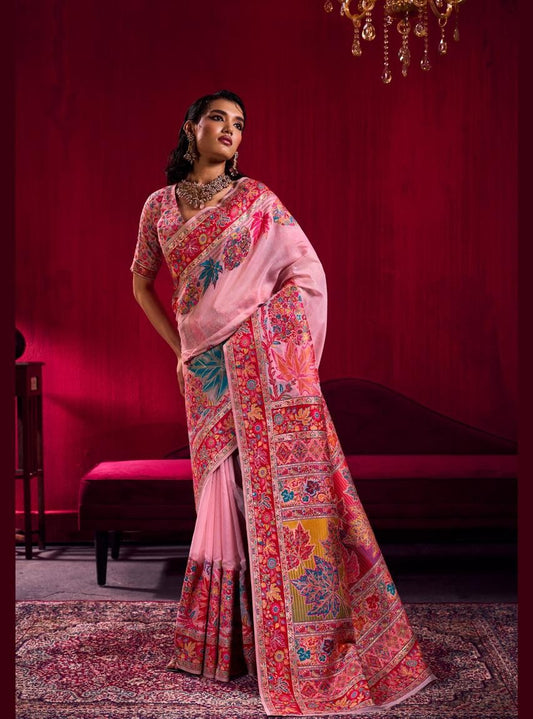 Woman wearing a pink saree with intricate patterns in a room with red walls.